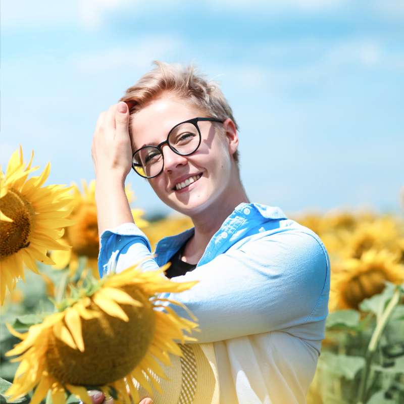 Eine Frau in einem Sonnenblumenfeld lächelt glücklich in die Kamera, was für den erfüllenden und blühenden Neuanfang im Pflegeberuf steht.