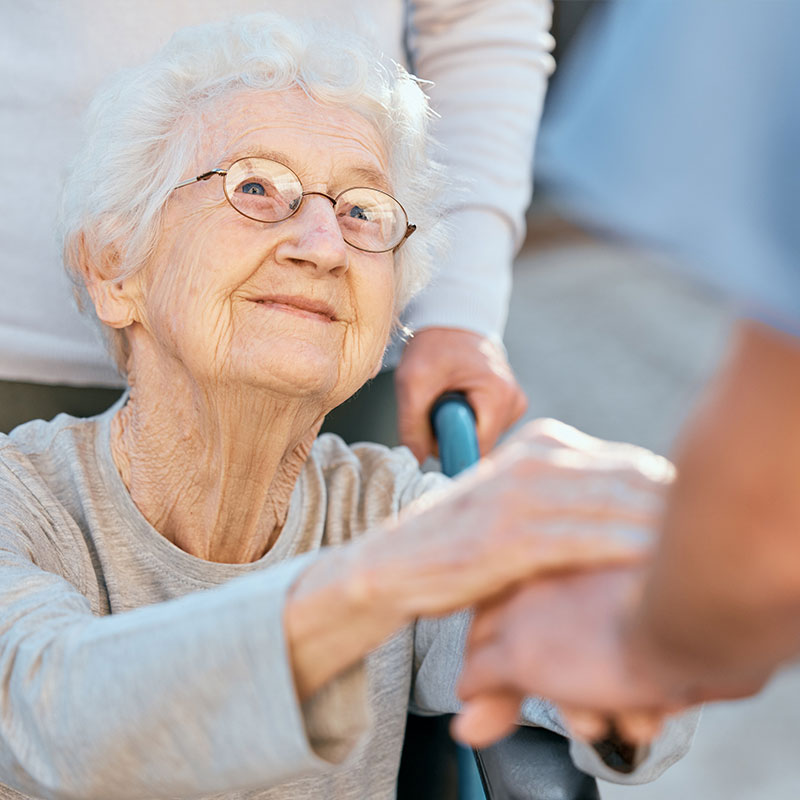 Pflegekraft kümmert sich einfühlsam um eine ältere Dame im Rollstuhl, im Grünen bei einem Spaziergang, Pflegedienst mit Herz.