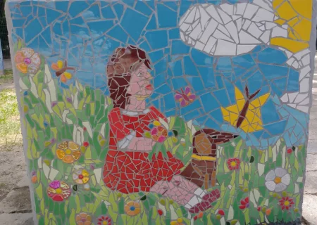 Ein Mosaik von Angelika Schaupp vom Pflegedienst AML zeigt ein Mädchen, das in einer blumenreichen Wiese sitzt. Das Kunstwerk, Teil des internationalen Mosaikprojekts, repräsentiert den ruhigen Herbst.