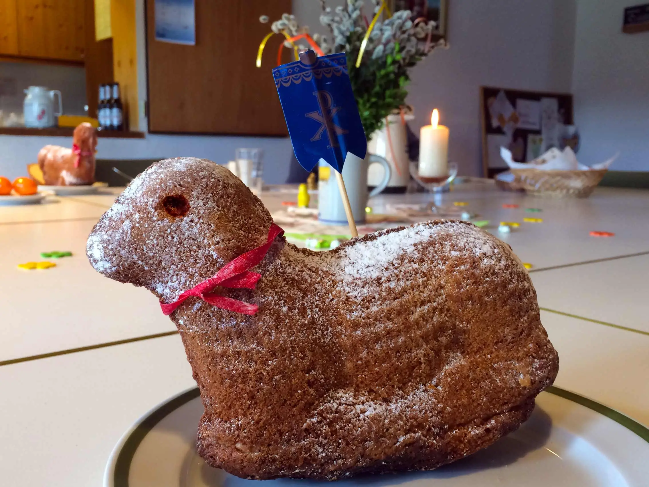 Ein traditionelles Osterlamm aus Kuchen, bestreut mit Puderzucker und mit einer Kerze geschmückt, auf einem festlich gedeckten Tisch im Sonnencafé.